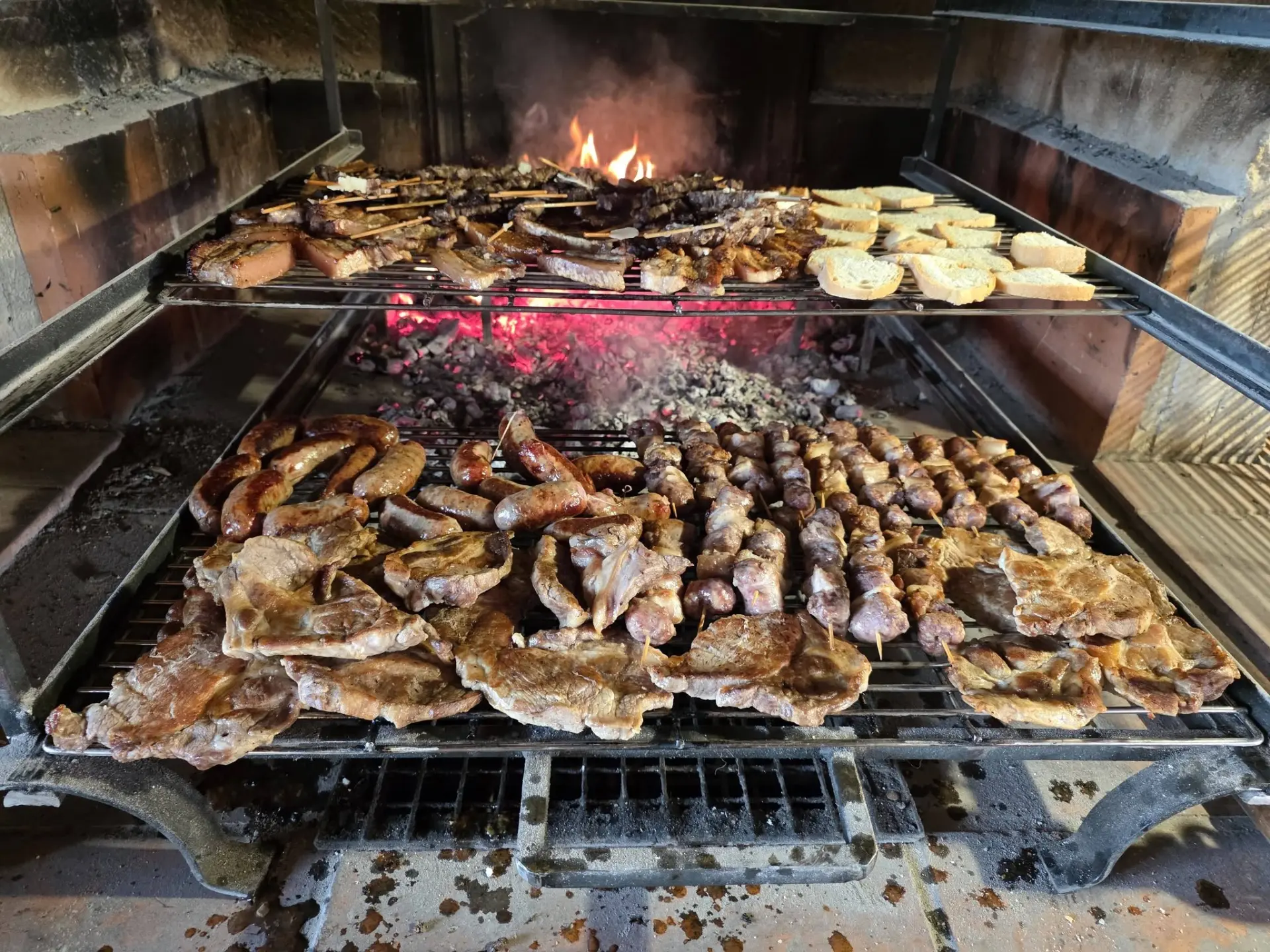 Griglia a legna a due piani carica di carne, salsicce e bruschette