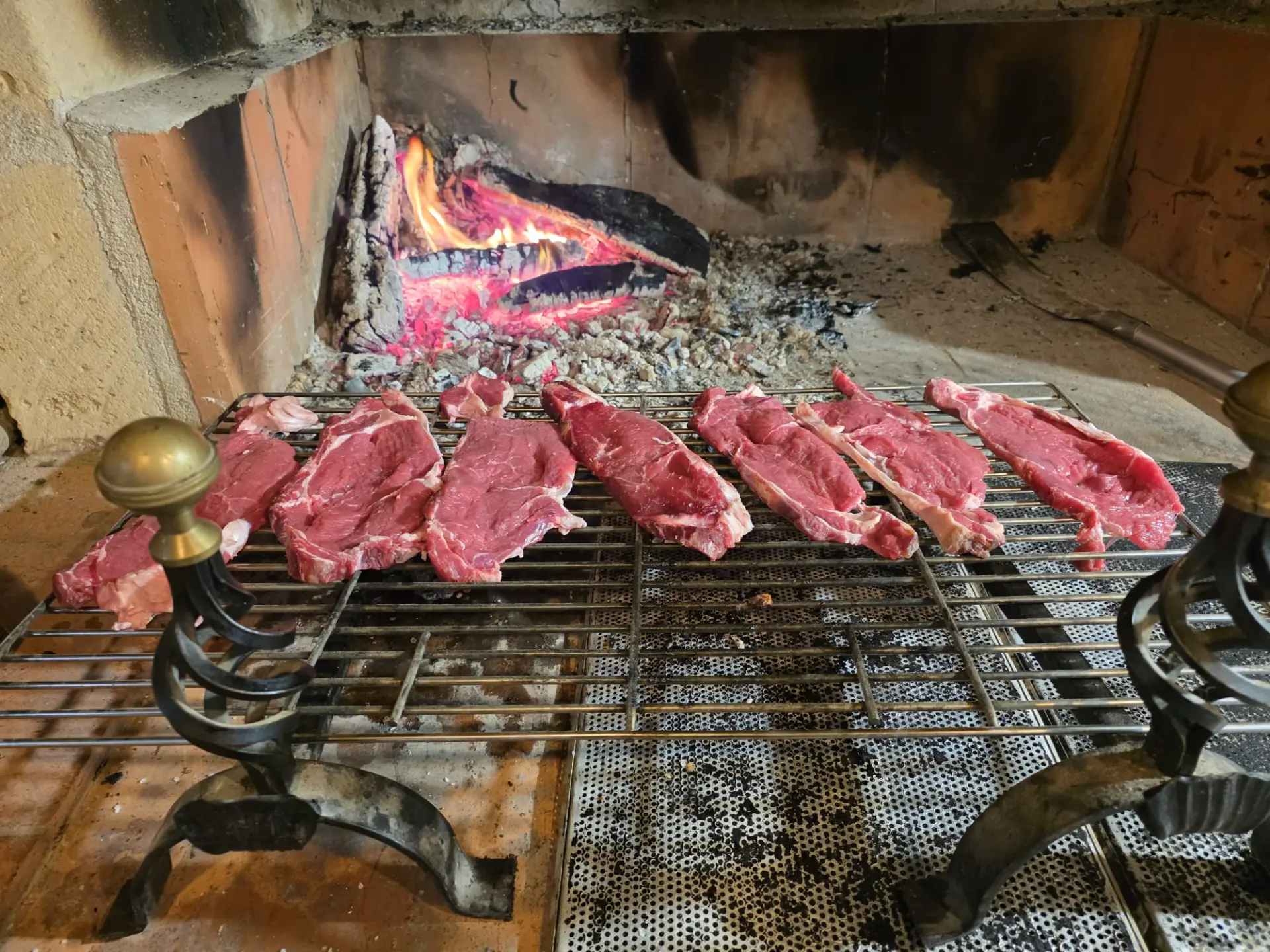 Fette di bistecca appena messe sulla griglia davanti al camino